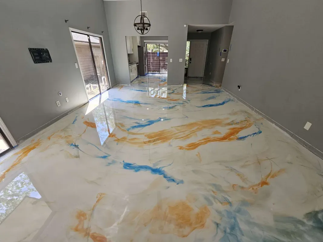 Large room with marbled white floor coated in blue and orange streaks, unfinished walls, and open doorways.