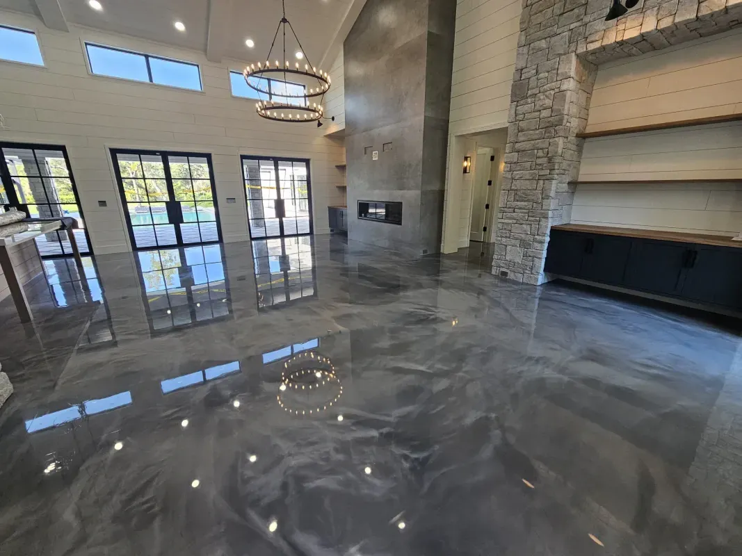 Modern living room with polished gray floors, tall windows, stone fireplace, and chandelier lighting