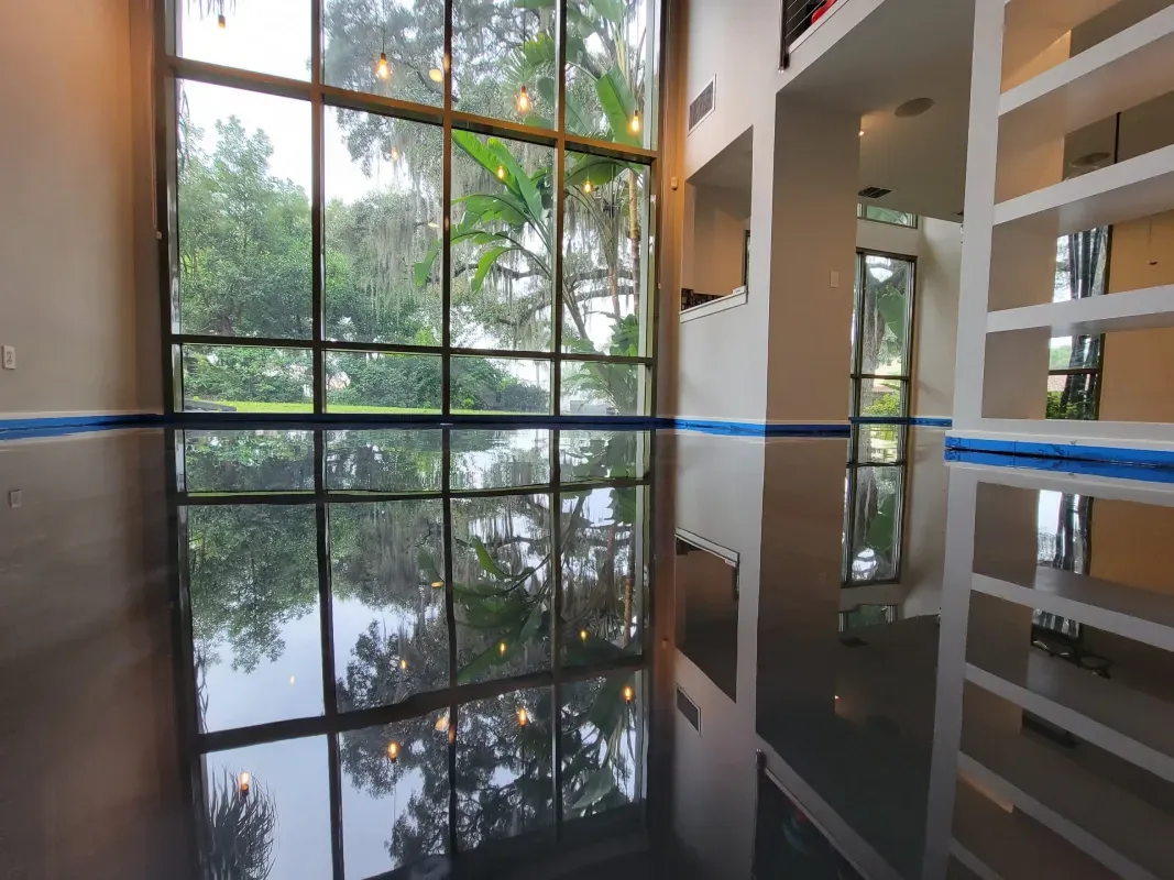 Modern interior with a tall window reflecting trees on a glossy floor, beside open shelving