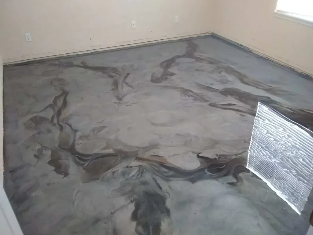 Small room with a wet, newly coated gray floor and a vent or fan near the corner.