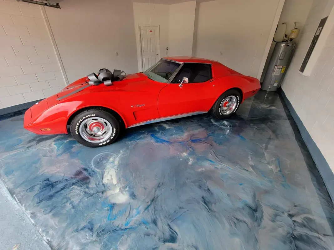 Red classic sports car parked in a garage with a blue floor and white walls