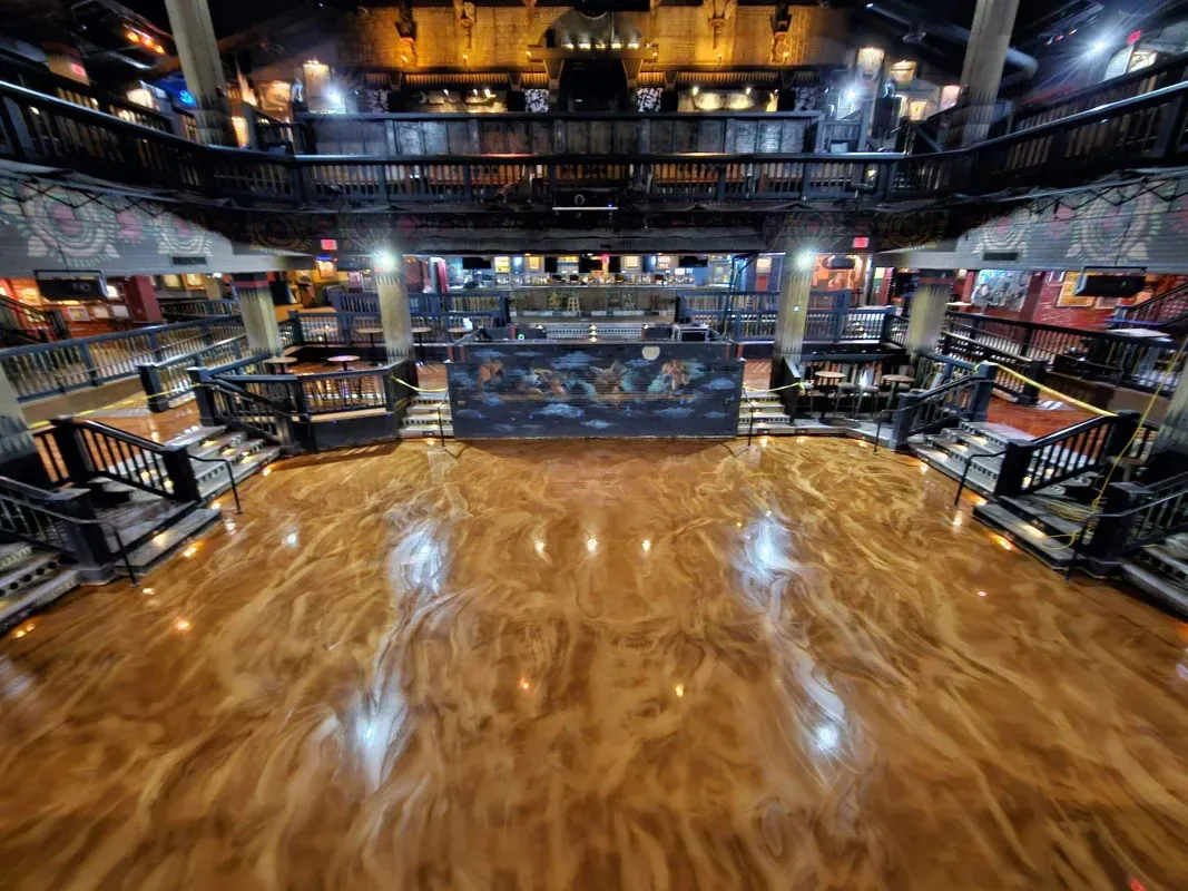 Empty indoor basketball court with a glossy wooden floor and spectator seating in the background