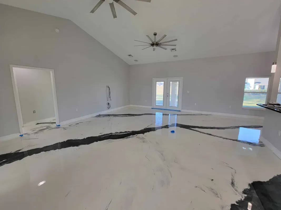 Spacious empty room with gray walls, white ceiling fans, and a glossy black-and-white floor under construction