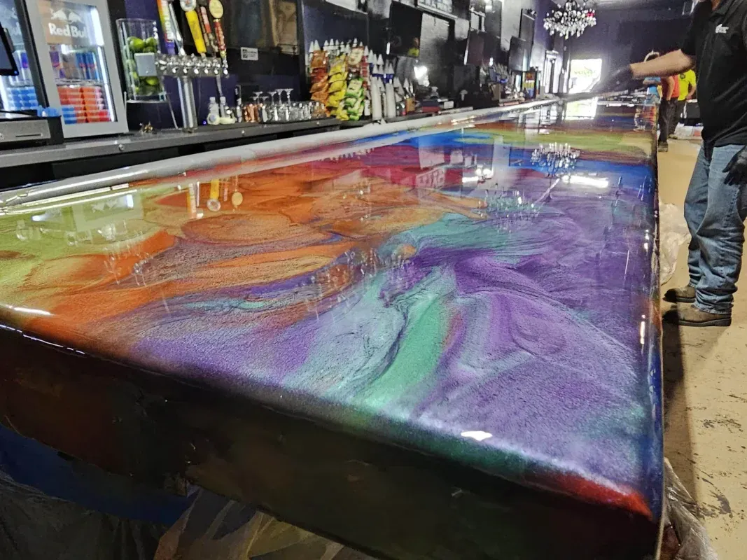 Colorful swirled resin coating a car body in a garage, with a person standing nearby