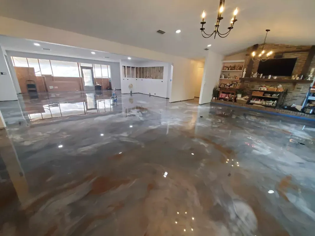 Empty modern room with glossy gray floor, chandeliers, and a kitchen/bar area in the background