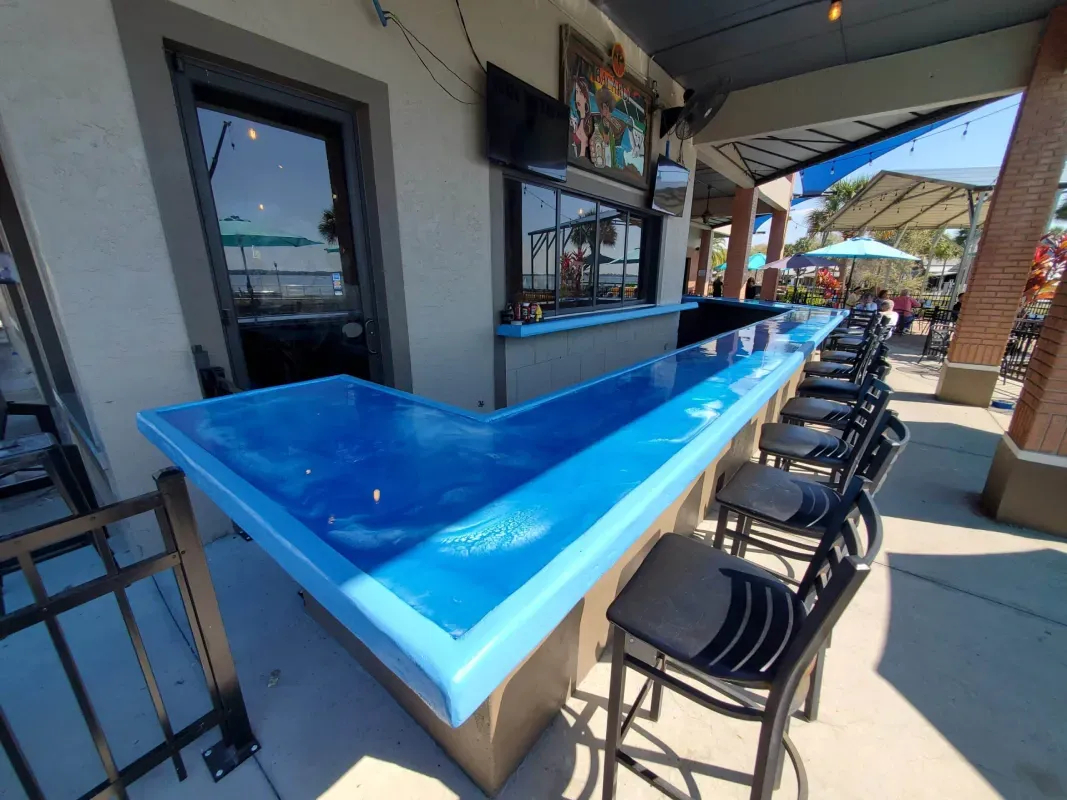 Blue triangular bar counter with stools on a sunny patio by the water