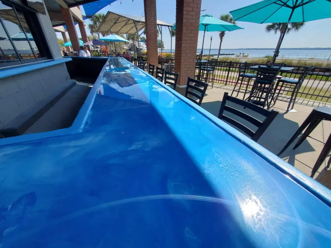 Blue rooftop bar counter with black stools and teal umbrellas overlooking a waterfront view