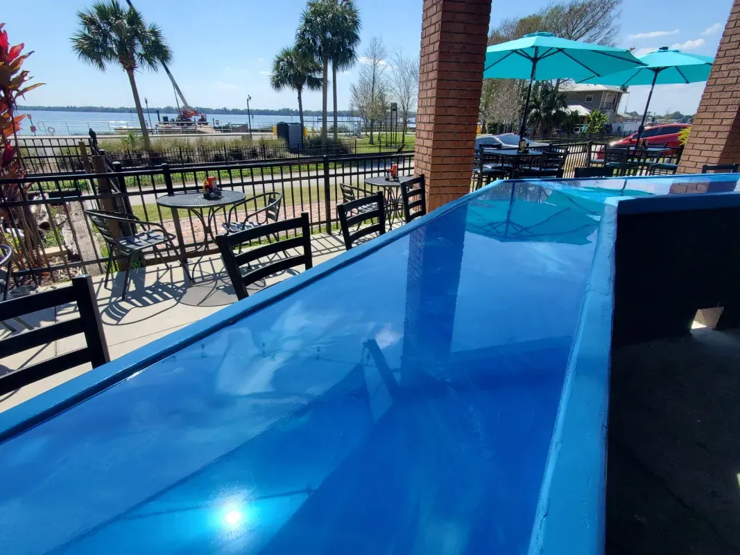Blue bar counter overlooking an outdoor patio with palm trees and a waterfront view.