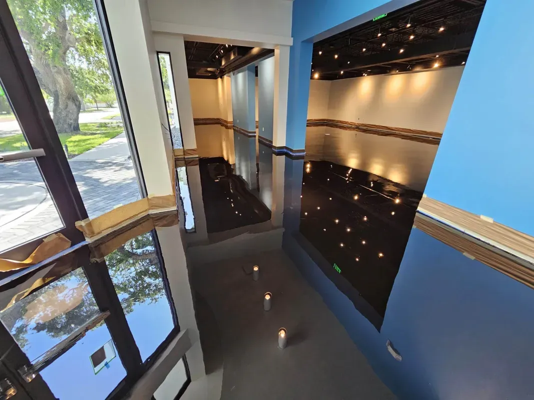 Modern hallway with glossy black floor, blue walls, recessed lighting, and glass doors overlooking greenery