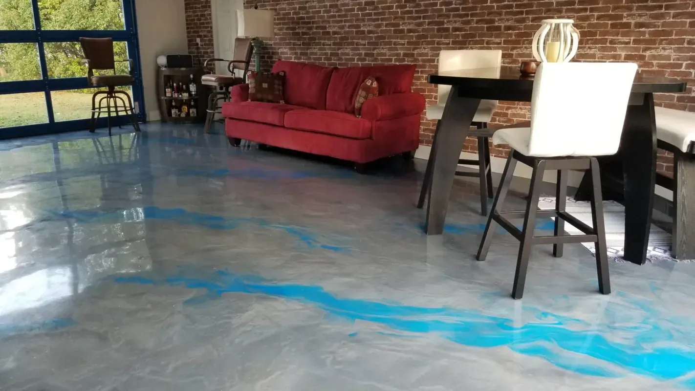 Modern room with a red sofa, bar stools, and blue epoxy floor beside large windows