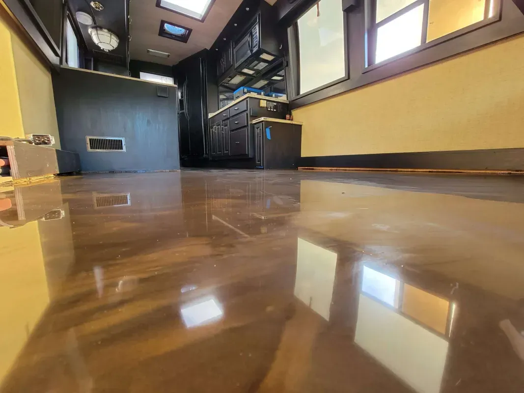 Low-angle view of a shiny wooden floor in a narrow, modern RV hallway with cabinets and windows.