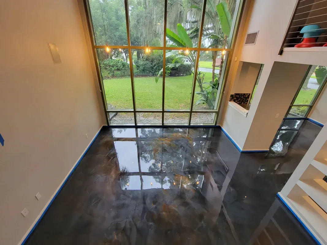 Modern room with glossy dark floor, large floor-to-ceiling windows, and a view of green backyard.