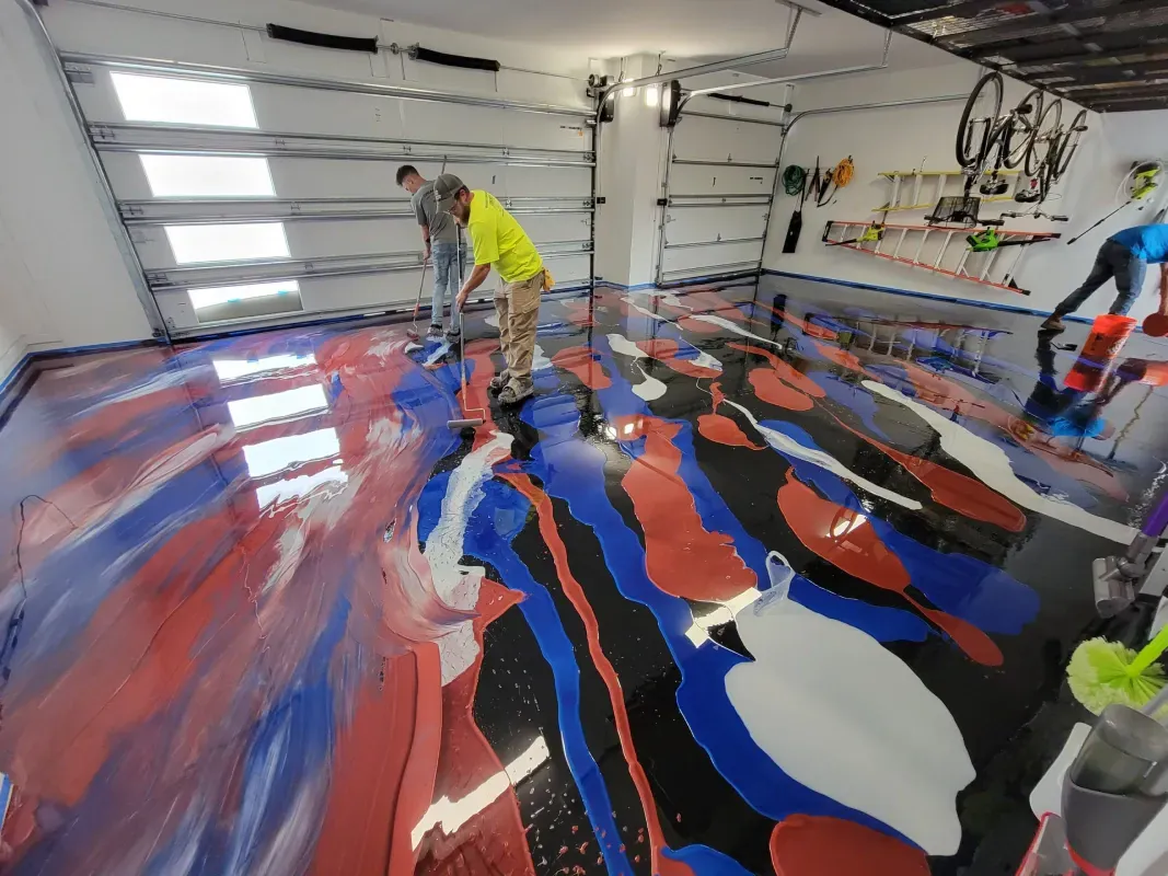 Workers pouring colorful epoxy floor coating in a garage.