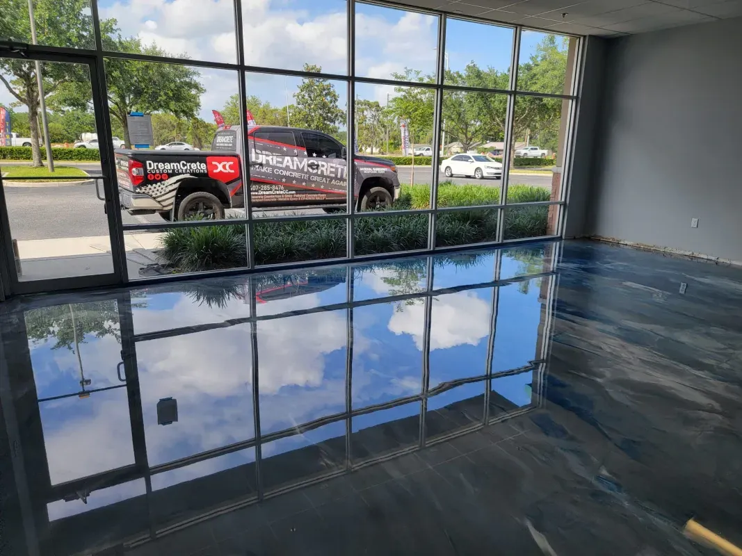 Empty room with flooded floor reflecting windows; red SUV parked outside a glass wall.