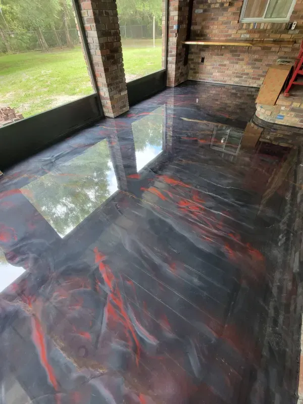 Glossy black and red epoxy floor in a covered porch with brick walls and large windows.
