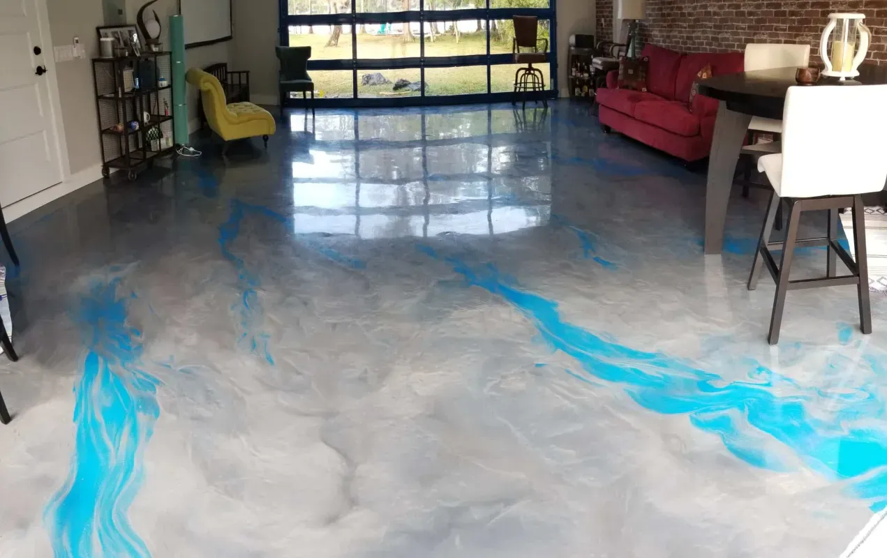 Living room with polished concrete floor and blue epoxy streaks, red sofa, yellow chair, and garage door at back