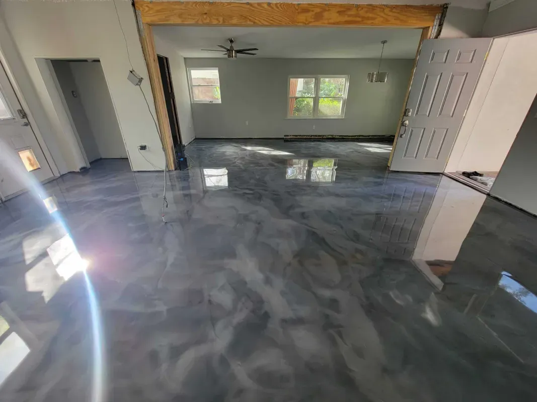 Empty living room with glossy gray floor, ceiling fan, windows, and open double doors to a hallway