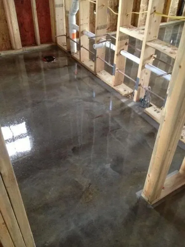 Shiny concrete floor in an unfinished room with exposed wooden wall framing and insulation storage shelves