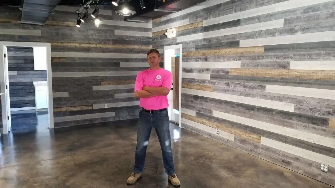 Person in a bright pink shirt standing in a modern room with wood-paneled walls and concrete floor.