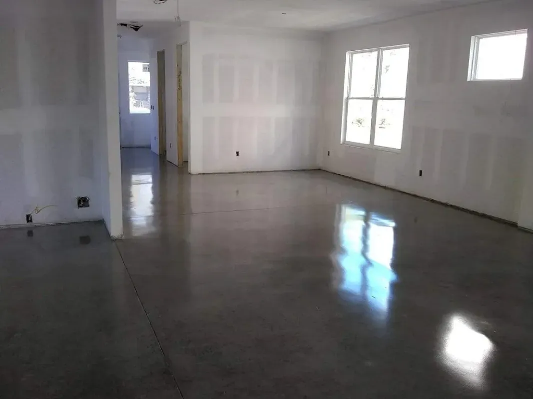 Empty unfurnished room with white walls, glossy concrete floor, and sunlight from windows