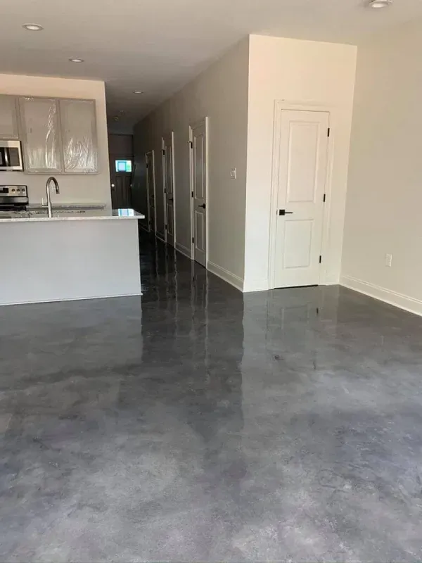 Empty modern apartment living area with gray concrete floor, kitchen counter, hallway, and white doors