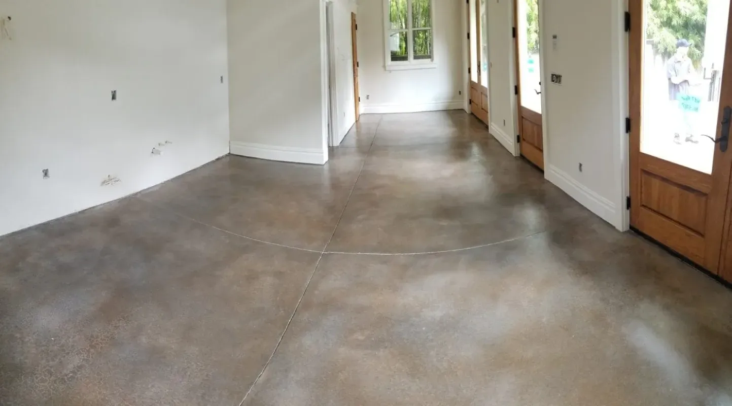 Empty concrete-floored hallway with white walls and wooden doors, lit by daylight from windows.