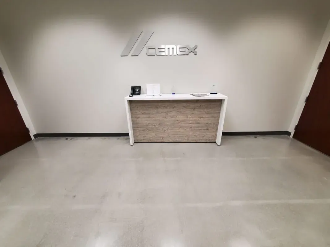 Empty Cemex reception area with white walls, a stone-front desk, and polished concrete floor.