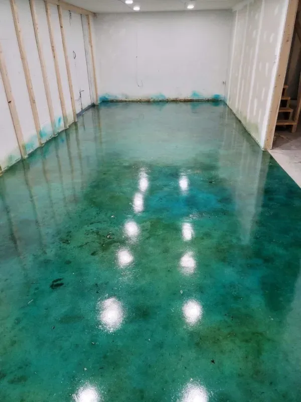 Glossy green epoxy floor in an empty basement or room with white walls and exposed framing