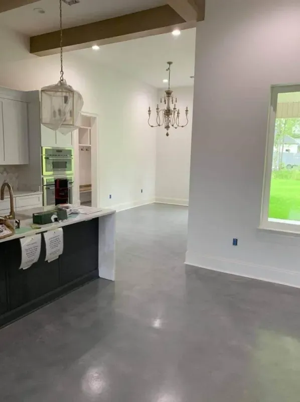 Empty modern kitchen and dining area with gray floors, white walls, and large windows.