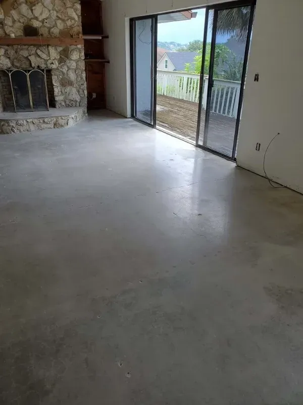 Empty living room with unfinished concrete floor, stone fireplace, and sliding glass doors to a balcony