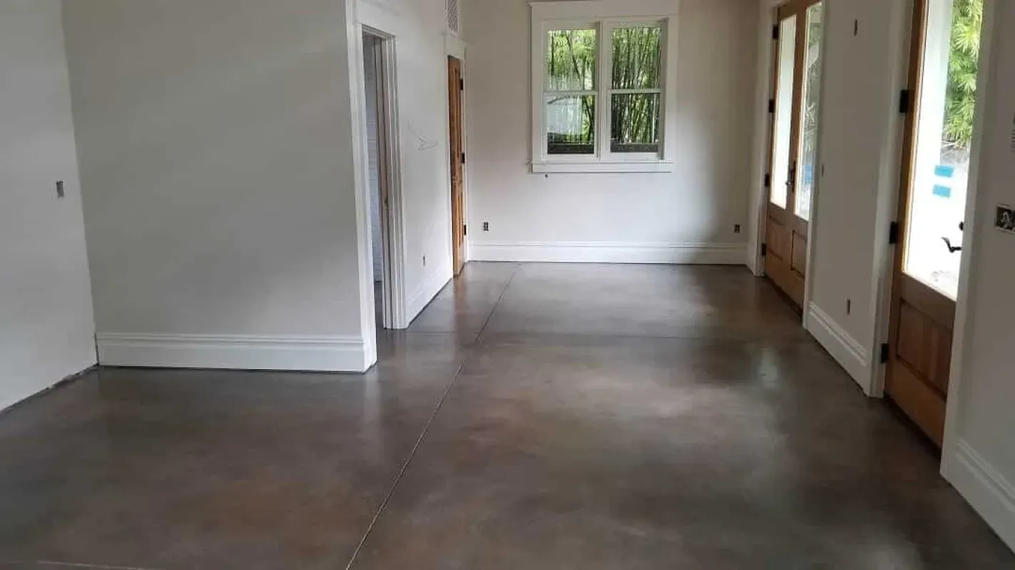 Empty room with dark concrete floor, white walls, and windows at the far end.