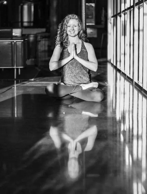 Woman meditating cross-legged on a glossy floor, hands together in prayer pose, with her reflection visible.