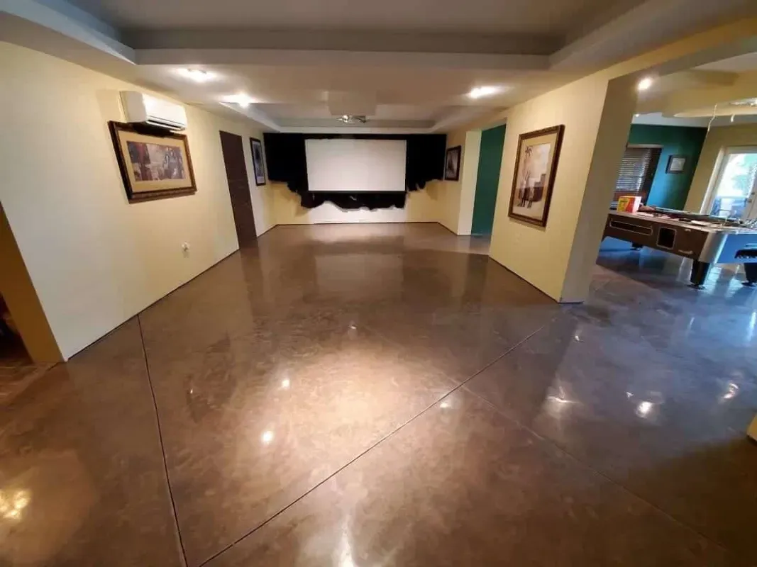 Wide empty living room with polished tile floor, beige walls, and a TV on the far wall.