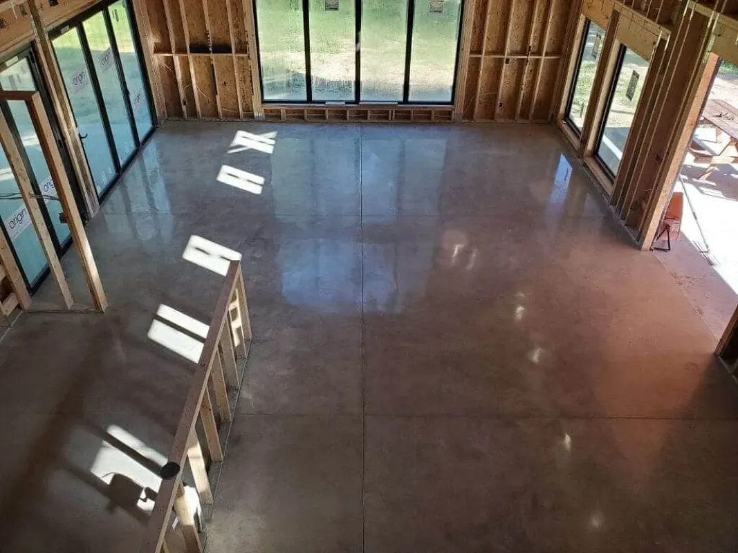 Empty sunlit room with large windows and a polished concrete floor under construction