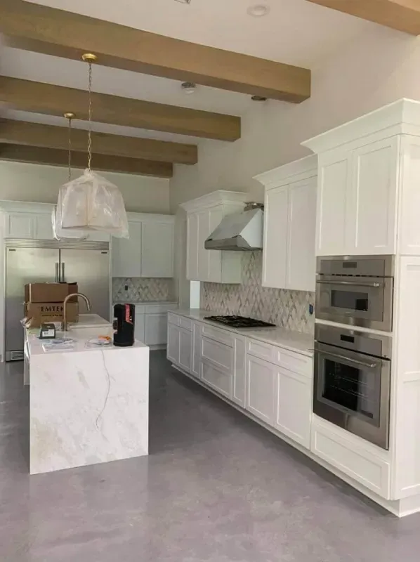 Modern white kitchen with island, wood ceiling beams, stainless appliances, and gray floor