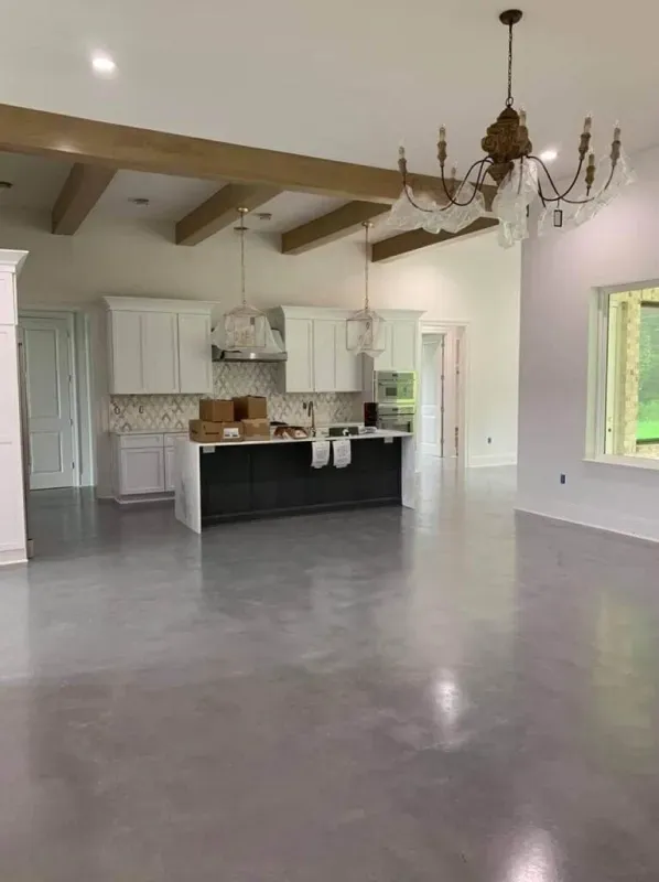 Spacious empty living room with polished concrete floor, white kitchen, exposed beams, and chandelier.