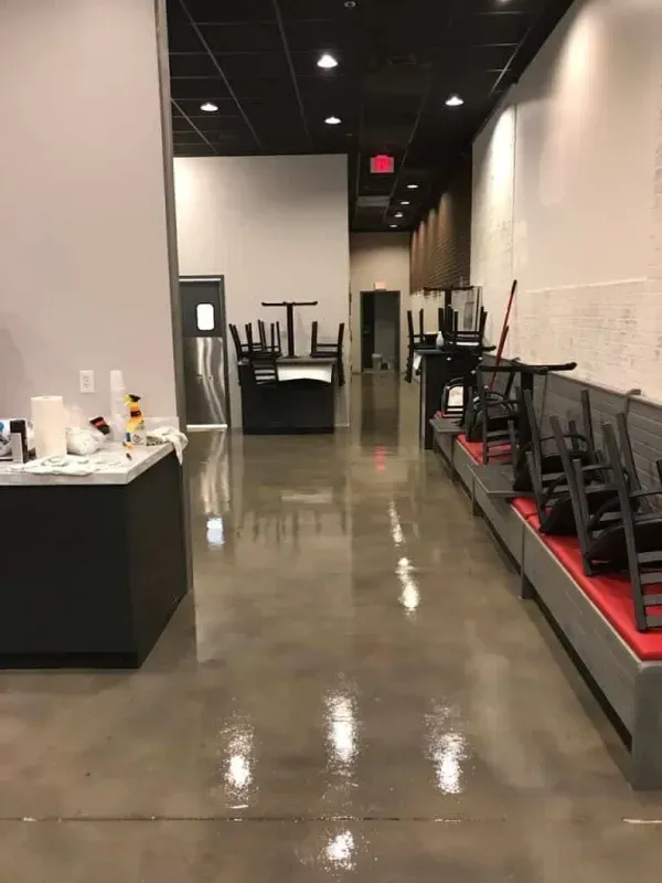 Empty restaurant interior with polished floor, black tables, and stacked chairs along the wall