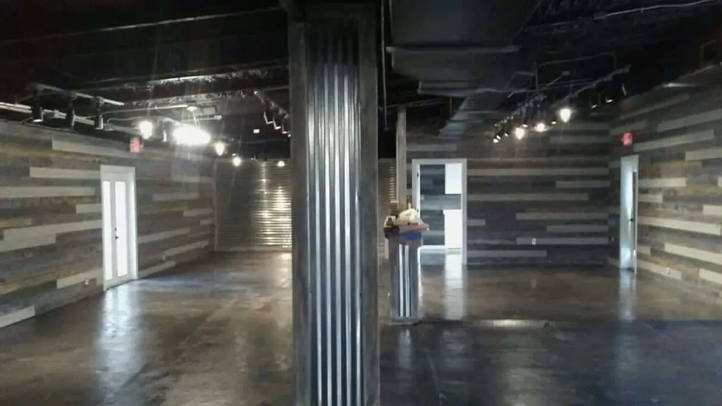 Dim industrial hallway with striped walls, a central black pillar, and a person standing near a doorway.