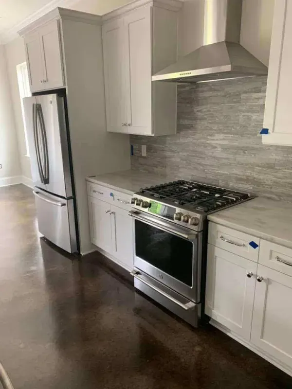 Modern kitchen with stainless steel appliances, white cabinets, gray tile backsplash, and dark wood floors