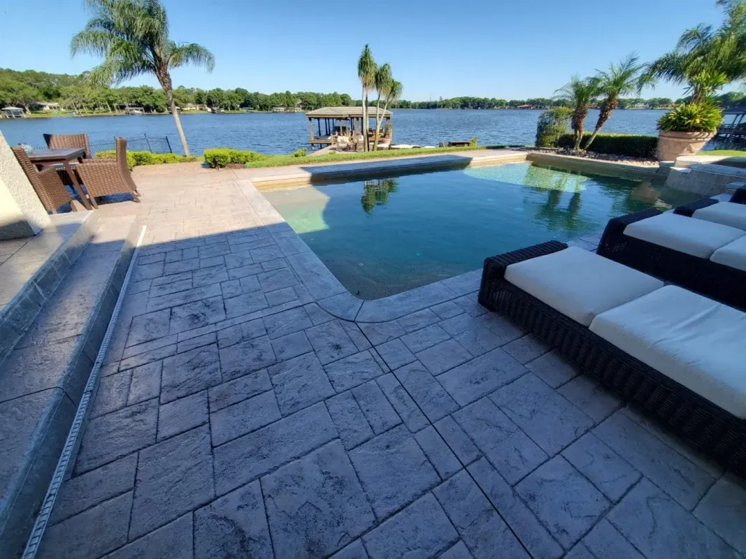 Backyard pool overlooking a lake, with lounge chairs and palm trees under a clear sky