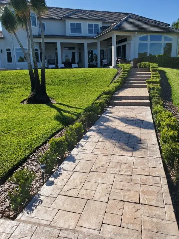 Front walkway leading to a large white house with a covered patio and green lawn.