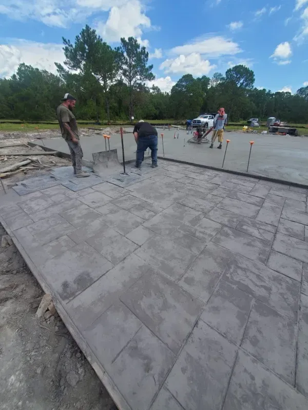 Workers smoothing a large concrete slab at an outdoor construction site under a partly cloudy sky