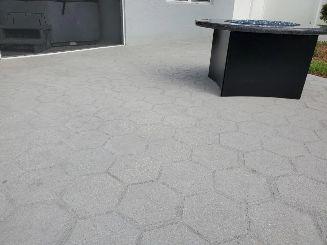 Outdoor patio with gray hexagon pavers and a black round table against a gray wall