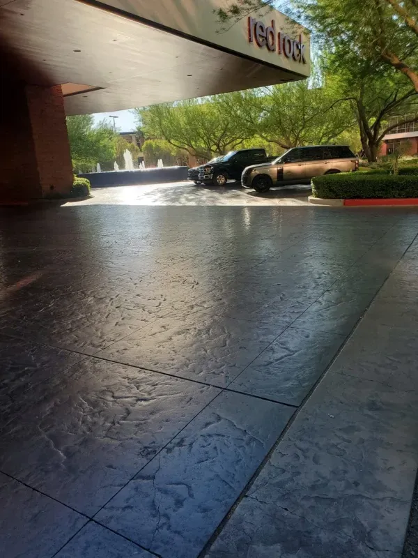 Covered hotel driveway with parked cars and sunlit trees beyond the entrance