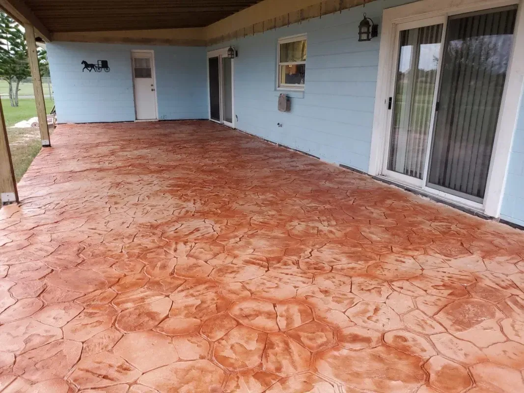Covered patio with reddish stamped concrete floor, light blue walls, and sliding glass doors.