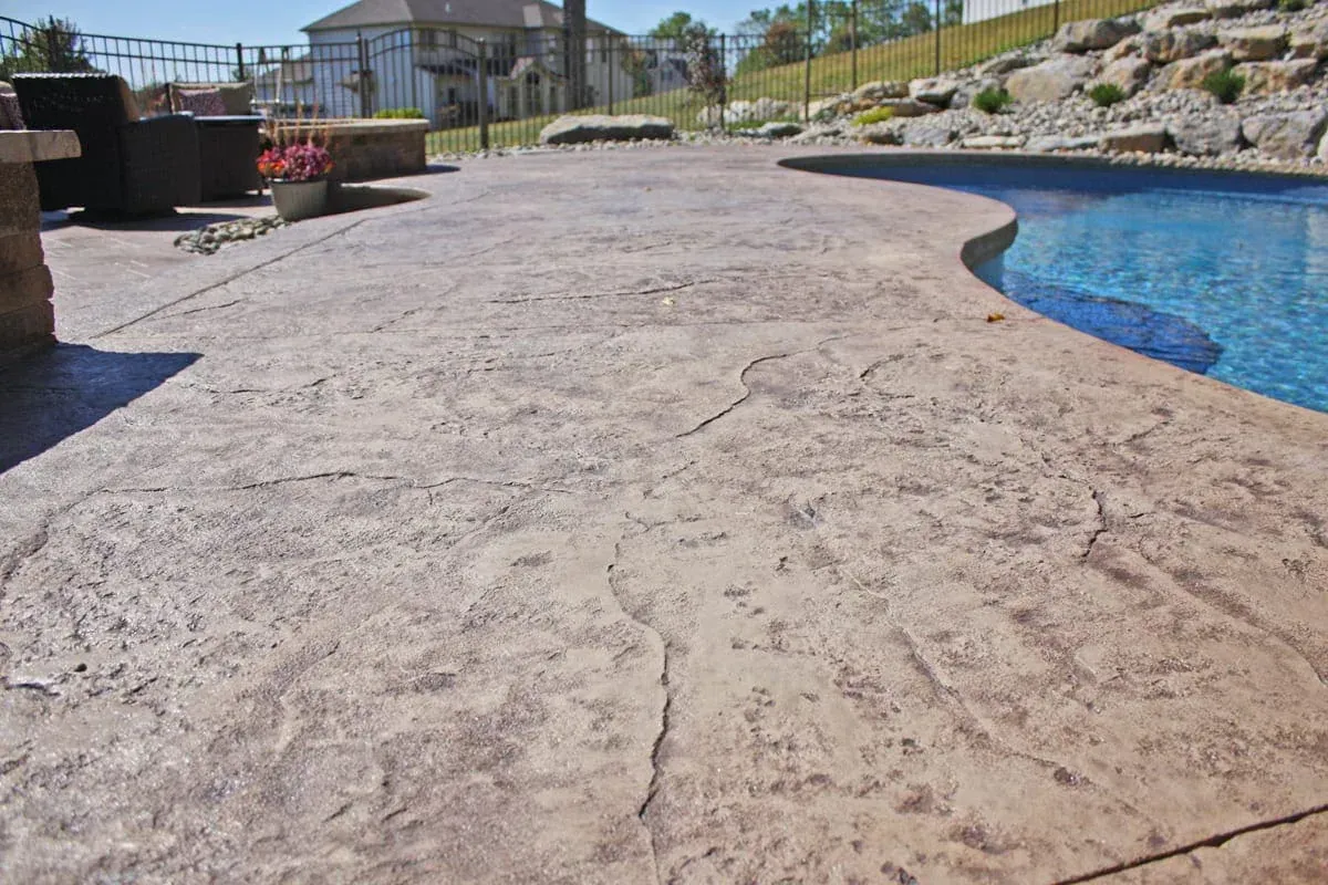 Curved stone pool deck beside blue swimming pool with rocks and landscaping