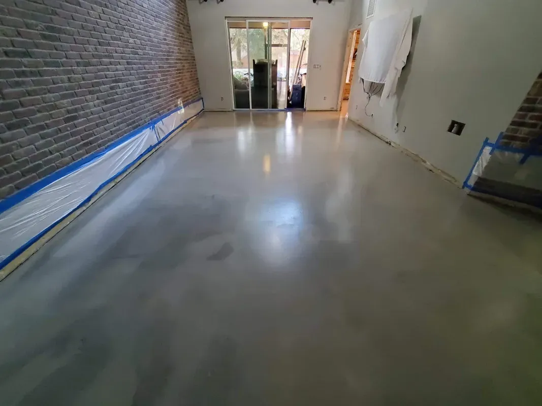 Empty hallway with polished concrete floor, brick wall on the left, and glass doors at the far end.