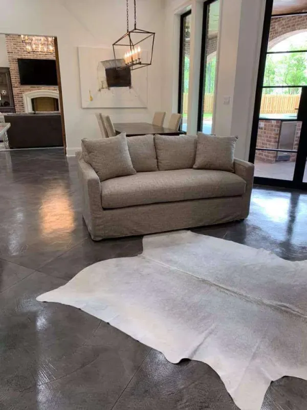 Living room with beige sofa and chair, large windows, dark polished floor, and a white hide rug on the floor