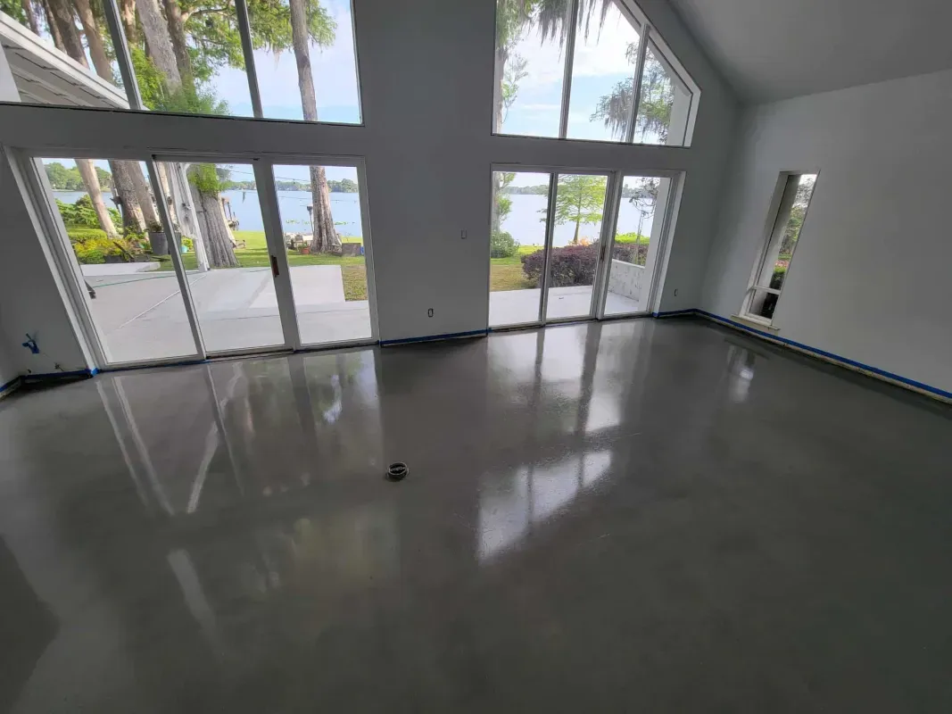 Empty modern room with glossy gray floor, large windows, and sliding glass doors opening to palm trees outdoors