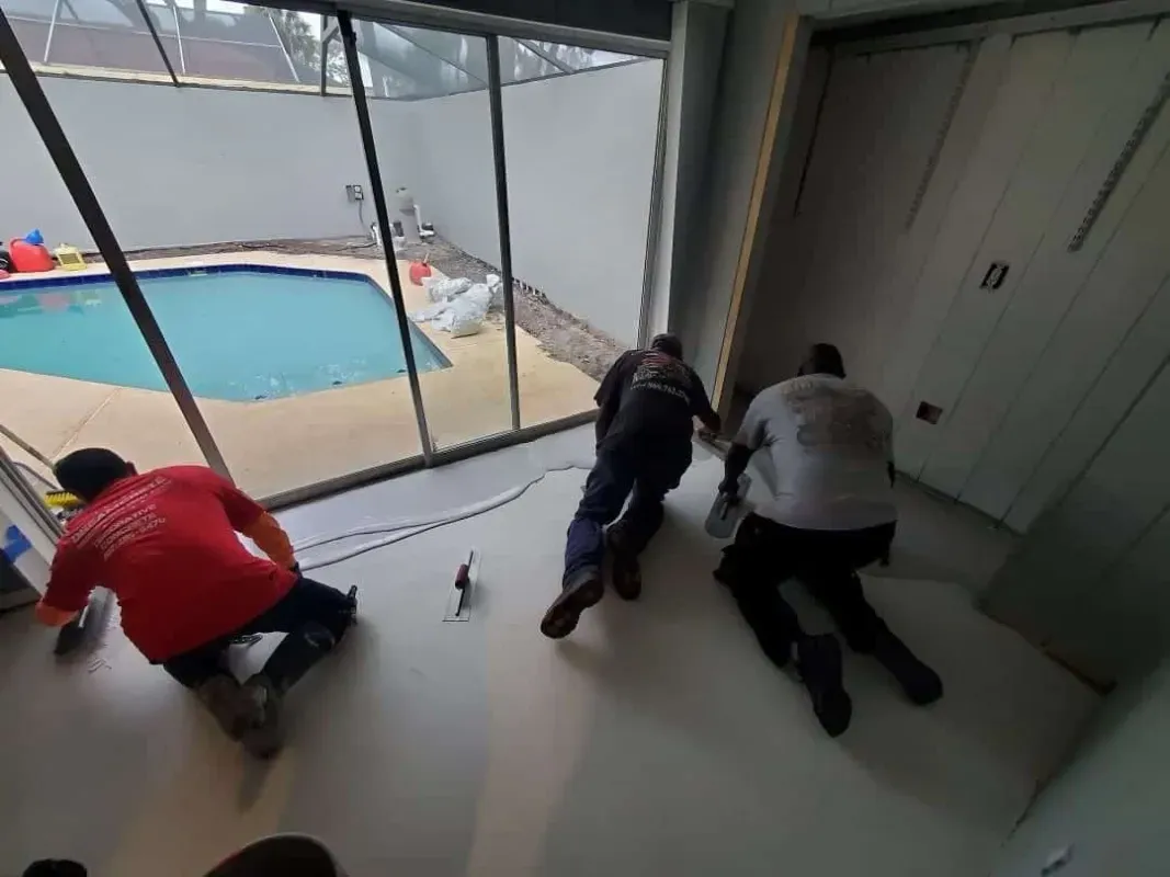 People kneeling on a room floor by large windows, looking out at a backyard pool and fallen snow.